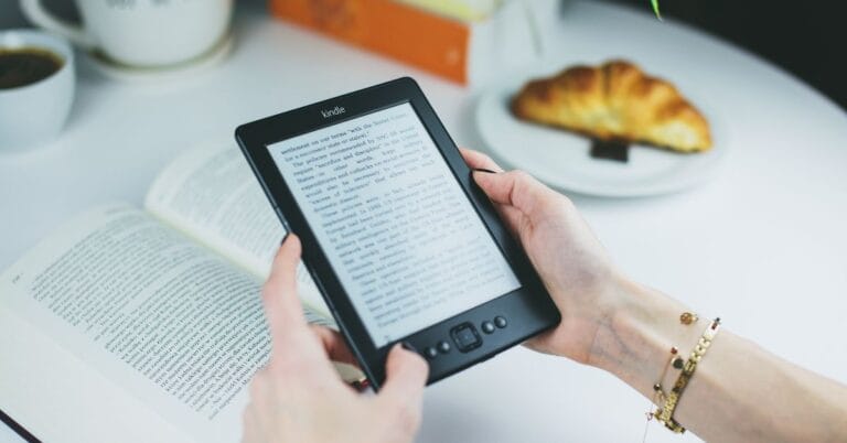 Pessoa segurando um Kindle em uma loja, com a tela inicial de carregamento visível, destacando o design leve e a tecnologia de tinta eletrônica do dispositivo.