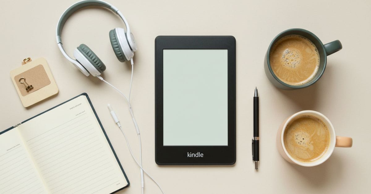 Kindle e-reader ao lado de uma xícara de café, fones de ouvido, caneta e caderno aberto sobre uma superfície clara, criando uma atmosfera acolhedora e inspiradora para leitura de livros-kindle-gratis.