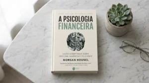 Livro A Psicologia Financeira de Morgan Housel sobre superfície de mármore — resenha completa e principais lições sobre comportamento financeiro em 2026.