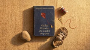 Livro O Caçador de Pipas de Khaled Hosseini sobre superfície arenosa com luz dourada — resenha completa do romance e do filme de 2007.